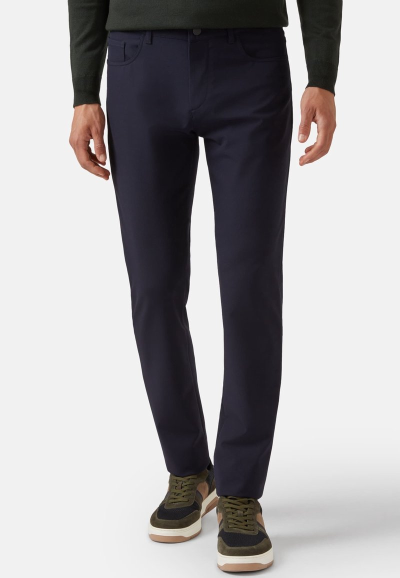 Pantalones elásticos en color marino con corte recto, que cuentan con bolsillos frontales y una textura suave, combinados con zapatillas oscuras.