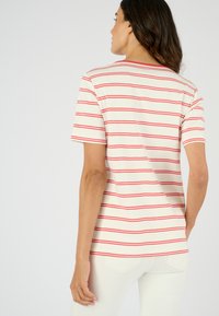Camiseta a rayas con rayas rojas horizontales sobre un fondo crema, de manga corta y corte relajado. Material de algodón, escote redondo.