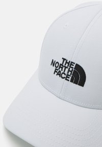 Vit keps av tyg med en strukturerad design, böjd skärm och svart broderad logotyp för The North Face på framsidan.