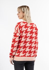 Pulover cu un model houndstooth roșu și roz, cu o croială lejeră, guler și mansete ribbate, confecționat dintr-un material tricotat moale.