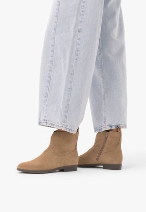 Jeans à jambes larges bleu clair associés à des bottines en daim marron clair avec des fermetures éclair latérales et des talons plats et bas.
