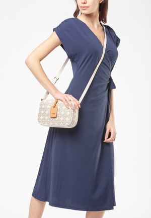 Navy wrap dress with short sleeves; smooth fabric drapes to mid-calf. Cream crossbody bag with geometric pattern and a tan tag.