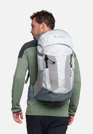 Zaino grigio chiaro con accenti testurizzati, spallacci regolabili e una cerniera frontale. Ideale per attività all'aperto, indossato da un modello.