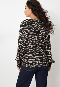 Blusa de manga larga con estampado de animal en negro y beige, que presenta un cierre de botón en la parte posterior y un detalle fruncido en el escote, combinada con jeans oscuros.