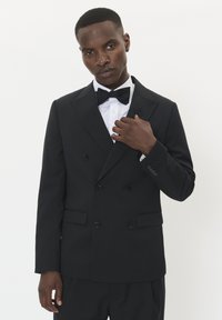 Melna divrindas smoking jaka ar klapām, apvienota ar baltu kreklu un melnu tauri. Gluda auduma un pielāgota piegrieze.