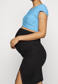 Modrý žebrovaný crop top v kombinaci s černou, upnutou sukní s bočními řasenými detailami a rozparkem až po stehna, který zvýrazňuje střední část těla.