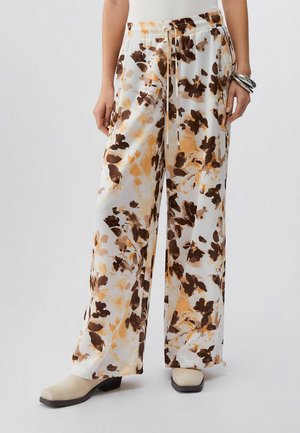 Wijde broek met bruine en beige bloemprint, elastische tailleband met trekkoord, gedragen met beige laarzen en zilveren armbanden.