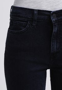 Jeans de mezclilla azul oscuro mostrados desde la cintura hacia abajo, con un primer plano de la cintura y los detalles de los bolsillos.