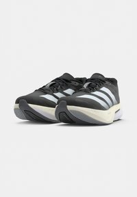Paire de chaussures de course Adidas noires et blanches avec trois bandes blanches et des semelles blanches épaisses sur un fond uni.
