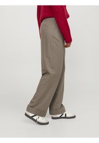 Breda, ljusbruna byxor med en slät textur och uppvikta muddar, kombinerade med vita sneakers med svarta ränder.