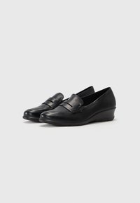 Black leather loafers with a decorative strap, rounded toe, and a low wedge heel. Smooth texture with subtle stitching details.