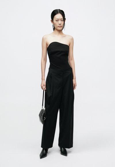 Haut noir sans bretelles associé à un pantalon noir taille haute. Accessoirisé avec un petit sac à main noir et des talons noirs pointus.