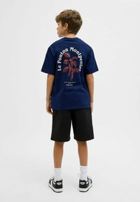 T-shirt en coton bleu marine avec un graphisme de plante orange et du texte au dos, associé à un short noir et des chaussettes blanches.