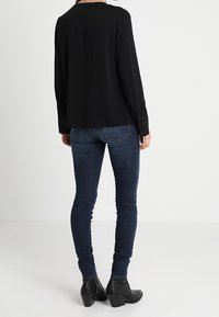 Blusa nera a maniche lunghe con taglio dritto e scollatura rotonda, abbinata a jeans skinny blu scuro e stivaletti neri con tacco.