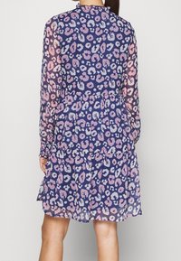 Långärmad, genomskinlig klänning med en marinblå bas och leopardtryck i rosa och ljusblått. Volangkrage och tierad design vid midjan.