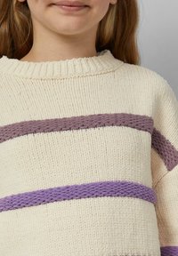 Kremowy sweter z teksturowanej tkaniny, z poziomymi paskami w jasnym i ciemnym odcieniu fioletu. Żebrowany dekolt i luźny krój.