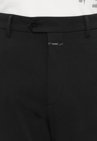 Crne krojene hlače s glatkom teksturom, zatvaranjem na gumb i malom oznakom s logotipom. Dizajnirane s čistim linijama i uskim krojem.