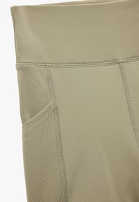 Jasnooliwkowe legginsy wykonane z elastycznego materiału, z szerokim pasem i bocznymi kieszeniami z płaskimi szwami dla większej trwałości.