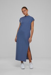 Rochie albastră până la genunchi, cu mâneci scurte și o fante laterală, realizată dintr-un material moale. Asortată cu adidași albi pentru un look casual.
