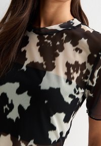 Blusa trasparente bianca e nera con motivo a macchie di mucca, caratterizzata da maniche corte e scollatura rotonda, realizzata in un tessuto leggero e testurizzato.