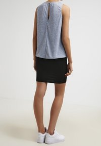 Šedý top bez rukávů s detaily otevřeného zadního výstřihu, v kombinaci s přiléhavou černou sukní. Model má na sobě bílé tenisky. Jemná struktura látky.