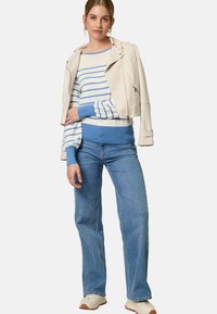 Giacca in pelle beige cropped su un maglione a righe blu e bianche. Jeans blu larghi e sneakers beige completano l'outfit.