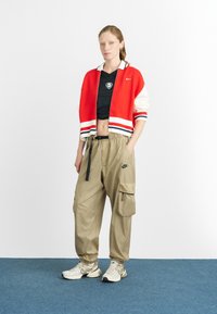 Cardigã vermelho e branco curto sobre um top curto de rede preto, combinado com calças cargo bege e ténis claros com detalhes cinzentos.