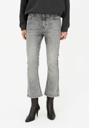 Personne portant un jean bootcut gris délavé, un top noir à manches longues et des bottines noires à talons aiguilles et bout pointu.