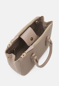 Beige handväska med en strukturerad design, slät textur, gyllene detaljer, dragkedja upptill och en avtagbar ficka inuti.