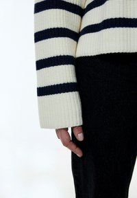Gebreide trui met witte en marineblauwe horizontale strepen, met een geribbelde textuur en wijde mouwen. Combinatie met donkere jeans.