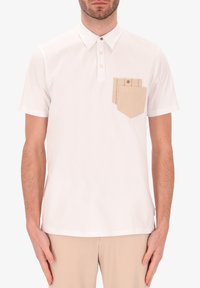 Polo shirt bianco a maniche corte con colletto a bottoni, caratterizzato da una tasca beige con un design a strati sul lato sinistro del petto.