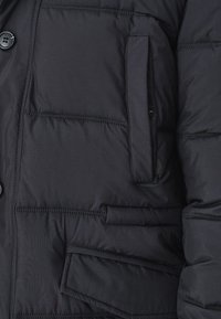 Granatowa kurtka puchowa z pikowanym wzorem, z zapięciem na guziki, kieszenią z klapą oraz miękką, izolującą teksturą materiału.