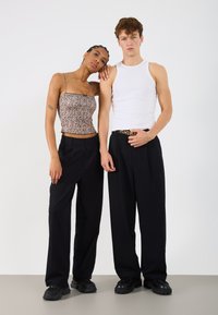 Μαύρο παντελόνι υψηλής μέσης και μπεζ μπλούζα με λεοπάρ μοτίβο, που διαθέτει λεπτές τιράντες; ανδρικό μοντέλο με λευκό αμάνικο μπλουζάκι και μαύρη ζώνη.