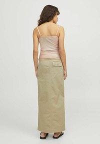 Camiseta sin mangas de canalé rosa claro con tirantes finos combinada con una falda larga beige que tiene un bolsillo trasero y un dobladillo recto. Sandalias negras.