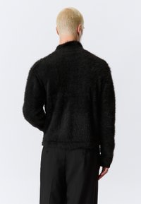 Μαύρο φόρμα με αφράτη υφή και άνετη εφαρμογή, με ψηλό γιακά και μακριά μανίκια. Το υλικό έχει απαλή, υφή με υφή.