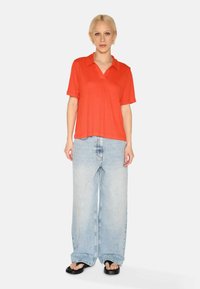 Rød kortærmet polo-shirt parret med løse lyseblå denim jeans. Overtøjet har en afslappet pasform og et enkelt design i glat stof.
