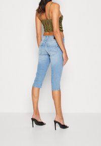 Green satin crop top with thin straps paired with light blue capri jeans. The jeans feature back pockets and a hemmed cuff. Black high-heeled mules.