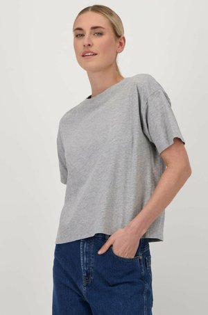 T-shirt gris à manches courtes avec une coupe décontractée, col rond et en coton doux. Porté avec un jean bleu foncé, présenté sur un fond clair.