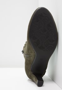 Kotníková bota z olivově zelené semiše s kuželovým podpatkem, bočním zipem a strukturovanou černou gumovou podrážkou s květinovým vzorem.