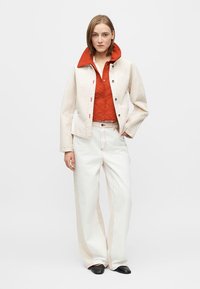 Ανοιχτόχρωμο τζιν μπουφάν με κόκκινη επένδυση καπιτονέ, σε συνδυασμό με φαρδιές λευκές παντελόνες και μαύρα παπούτσια. Διαθέτει ραφές σε αντίθεση και κουμπιά τύπου σναπ.