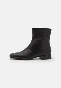 Botín negro de cuero hasta el tobillo con punta afilada, textura suave, diseño minimalista y tacón bajo en bloque. La cremallera lateral sube hasta el tobillo.