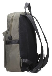 Zaino in tessuto verde con imbottitura in rete nera, tasche laterali e spallacci regolabili. Presenta un logo sulla tracolla; chiusura con zip in cima.