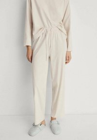Set de loungewear bej deschis, cu mâneci lungi și pantaloni cu talie elastică. Material moale cu o croială relaxată. Asortat cu papuci din fetru bleu deschis.
