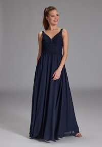 Abito da sera blu navy con bustier in pizzo aderente e gonna fluida, caratterizzato da una scollatura a V e spalline larghe. Tessuto morbido e leggero.