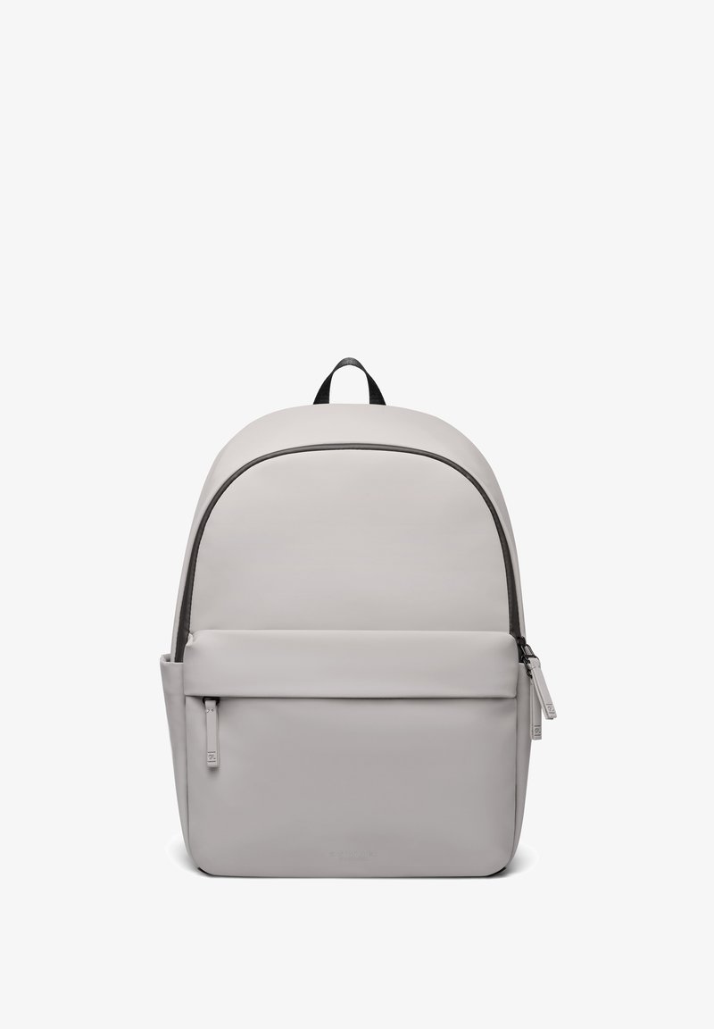 Sac à dos minimaliste gris avec poche avant zippée, compartiment principal zippé et poignée supérieure noire sur fond blanc.