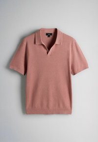 Polo en maille rose poudré à manches courtes avec col ouvert et tissu à texture fine, posé à plat sur une surface grise.