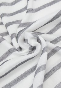 Hvit tekstil med brede grå striper, myk tekstur og et vevd mønster, arrangert i en spiralform.