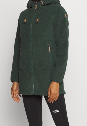 Donkergroen fleecejack met rits en capuchon, trekkoorden en met rits afgesloten zakken, gedragen over zwarte leggings met het logo van The North Face.