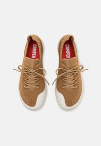 Braune gestrickte Sneakers mit einer weißen Gummisohle, die einen hohen Kragen und Schnürsenkel aufweisen. Rote Einlegesohlen präsentieren den Markennamen "CAMPER."