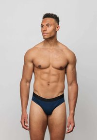 Dunkelblaue Baumwollslips mit einem schwarzen Gummibund, die eine glatte Textur und ein konturiertes Vorderdesign aufweisen.